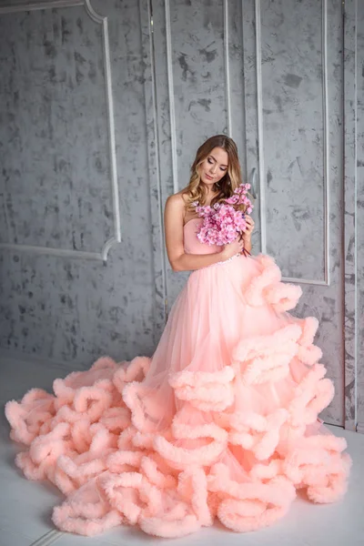 Hermosa joven con el pelo ondulado largo sosteniendo un ramo de flores en vestido rosa-la nube está en el interior — Foto de Stock