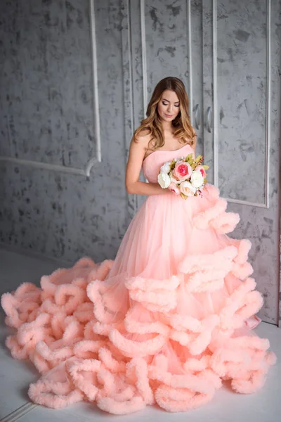 Hermosa joven con el pelo ondulado largo sosteniendo un ramo de flores en vestido rosa-la nube está en el interior — Foto de Stock