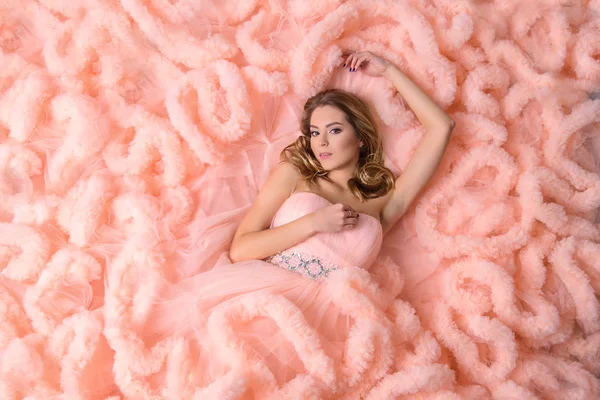 Hermosa joven con el pelo ondulado largo se encuentra en el vestido rosa-la nube me mira, vista desde arriba — Foto de Stock