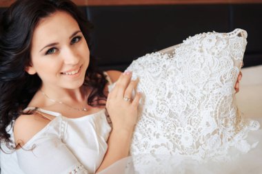 Gelin yatakta oturur ve gelinlik elinde tutar