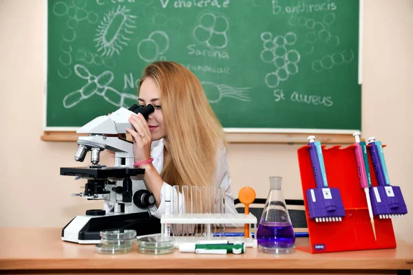 Mulher estudante bonita em um laboratório que trabalha com microscópio . — Fotografia de Stock