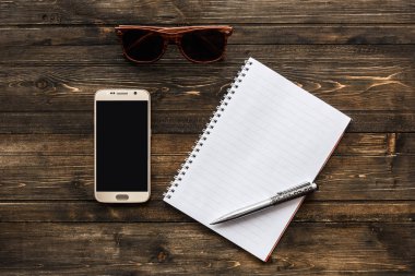Ahşap arka plan üzerinde not defteri, telefon kalem ve güneş gözlüğü Üstten Görünüm