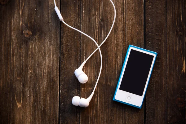 white earphones and blue music player on wooden background