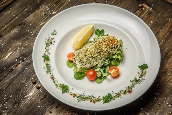 Bistecca di pesce con erbe aromatiche, limone, pomodorini e spezie su un piatto bianco fondo di legno — Foto Stock