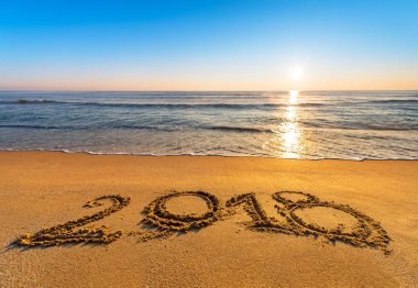 Number 2018 written on seashore sand at sunrise. Concept of upco clipart