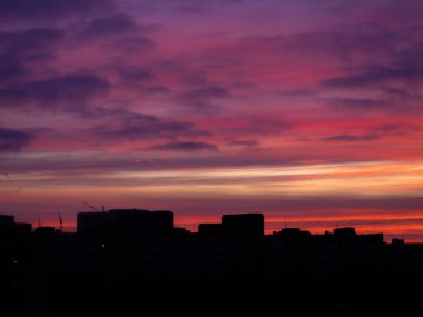 Güneşin doğuşunda binaların panoramik siluetinin üzerinde renkli bulutlu destansı gökyüzü. Moskova şehir silüeti, sabah manzarası.