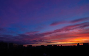 Güneşin doğuşunda binaların panoramik siluetinin üzerinde renkli bulutlu destansı gökyüzü. Moskova şehir silüeti, sabah manzarası.