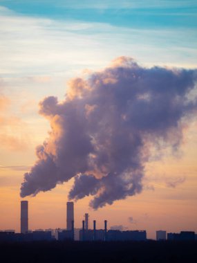 Endüstriyel fabrikadan bacalar ve karanlık ormanın arkasındaki uzak binalar tütütüyor. Gün batımında renkli alacakaranlık gökyüzü olan şehir manzarası silueti. Moskova şehri, Rusya.