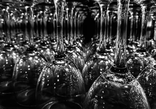 Close up upturned wine glasses on shelf on black background. Rows of the transparent stemware with reflections. Selected focus.