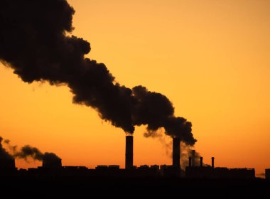 Endüstriyel santralin yüksek bacalarından siyah duman bulutlarının siluetleri ve arka plan olarak berrak gün batımı gökyüzü. Alacakaranlık gökyüzü ile şehir manzarası silueti.