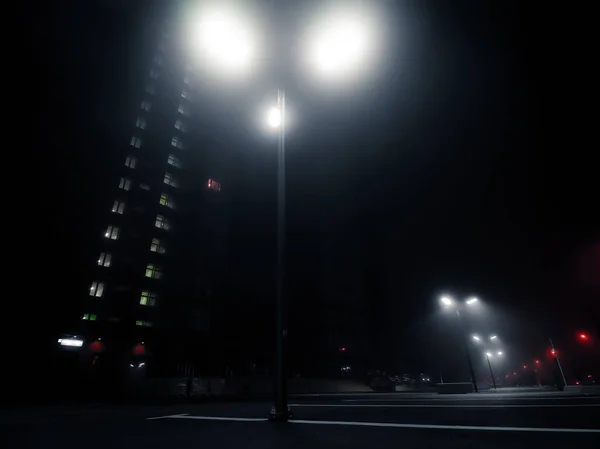 Cyberpunk style urban landscape. Empty parking with tall lamp posts near skyscraper in the night. Bottom view. Modern street lights in the fog on empty parking near residential apartment building.
