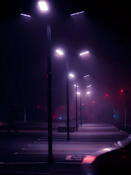Modern street lights in the fog on empty parking in the night and fragment of the blurred car silhouette on foreground. Cyberpunk style shot. Empty parking in the night. Moscow city, Russia.