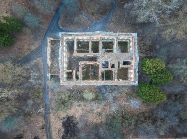 Terk edilmiş, çatısı olmayan eski tuğla binanın havadan görünüşü kat planına benziyor. Konağın tepeden aşağı insansız hava aracı manzarası. Etrafı ağaçlar ve kaldırımlarla çevrili. Bahar mevsimi.