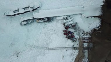 Donmuş rıhtımın üzerinde dikey tırmanış. Gemiler ve botlar beyaz buza bulanmış. Kış mevsiminde Baykal Gölü 'nün Olkhon adası kıyı şeridi ve buz yüzeyi havadan aşağı görünüyor..