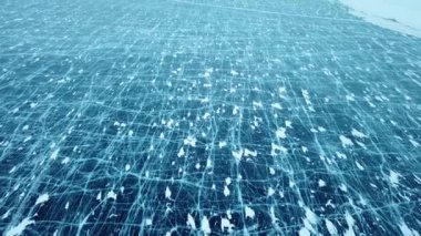 Sibirya 'da (Rusya) donmuş bir Baykal gölünün kalın katı tabakasında çatlaklarla buz yüzeyinde yatay uçuş. Yırtık ve karlı buzlu manzara, havadan çekim..