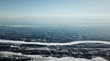 Kış mevsiminde Baykal Gölü 'nün havadan panoramik manzarası. Örümcek ağı donmuş buz yüzeyinde ve açık mavi gökyüzünün altında ufukta görünen dağda çatlar. Yukarıdan perspektif görünümü.