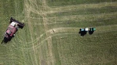 Aerial drone view of the farm work: grain harvesting. Red combine maneuvers on the field near tractor with large round baler at the field. Penza region, Russia.
