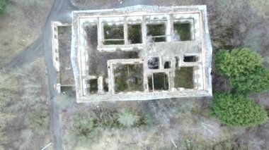 Terk edilmiş malikâne harabelerine yavaş yavaş iniyor. Yukarıdan aşağıya insansız hava aracı görüntüsü ve yakınlaştırma etkin. Terk edilmiş, çatısı olmayan eski tuğla binanın havadan görünüşü park planıyla çevrili gibi görünüyor..
