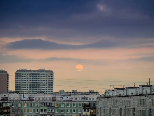Gökyüzü bulutlu ve şehir merkezindeki apartmanların üzerinde yükselen ay var. Karanlık çöktükten sonra şehrin manzarası. Moskova şehri, Rusya. Suluboya resmine benziyor..