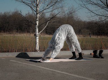 Salgın sırasında hayat. Koruyucu giysili, maskeli ve eldivenli bir kadın boş şehir parkında yoga egzersizleri yapıyor. Yaz sezonu, seçici odaklanma. Coronavirus (covid-19) salgını sırasında yaşam tarzı ve spor.
