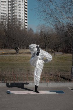 Salgın sırasında hayat. Koruyucu giysili, maskeli ve eldivenli bir kadın boş şehir parkında yoga egzersizleri yapıyor. Yaz sezonu, seçici odaklanma. Coronavirus (covid-19) salgını sırasında yaşam tarzı ve spor.