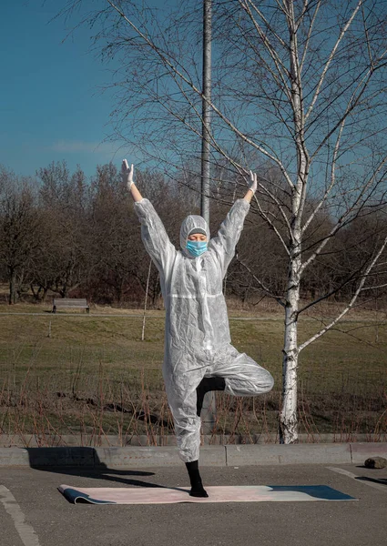Salgın sırasında hayat. Koruyucu giysili, maskeli ve eldivenli bir kadın boş şehir parkında yoga egzersizleri yapıyor. Yaz sezonu, seçici odaklanma. Coronavirus (covid-19) salgını sırasında yaşam tarzı ve spor.