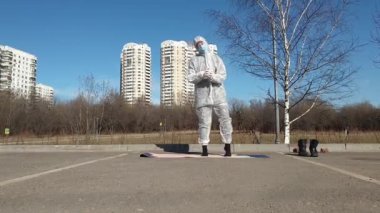 Salgın sırasında hayat. Koruyucu giysili, maskeli ve eldivenli bir kadın boş şehir parkında yoga egzersizleri yapıyor. Coronavirus (covid-19) salgını sırasında yaz mevsimi, yaşam tarzı ve spor.