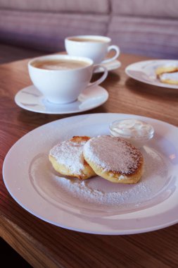 Gurme kahvaltısı, süzme peynirli krep, şurup. Beyaz tabak ve kapuçino ile pudra şekerli Ukrayna yemeği