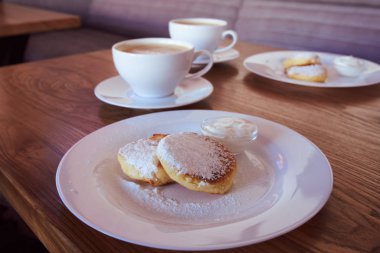 Gurme kahvaltısı, süzme peynirli krep, şurup. Beyaz tabak ve kapuçino ile pudra şekerli Ukrayna yemeği
