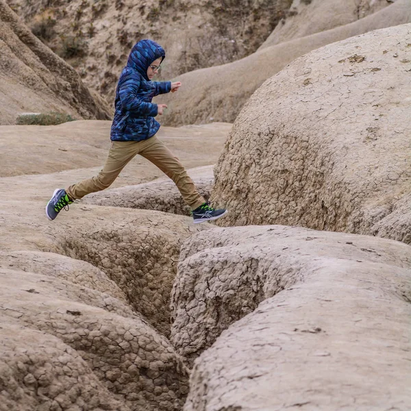 Niño saltando sobre tierra seca cubierta de grietas. Niño saltando —  Fotos de Stock