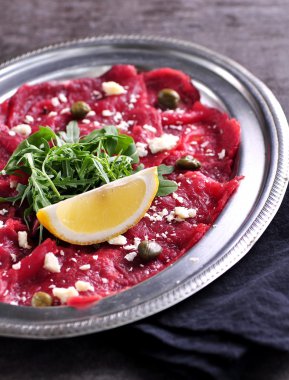 Carpaccio kapari, parmesan, roka, limon ve zeytin yağı ile sığır eti.