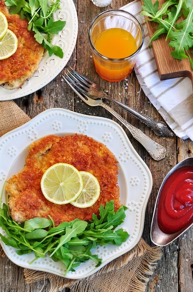 Schnitzel de cerdo con rúcula orgánica y lima sobre un fondo de madera viejo . — Foto de Stock