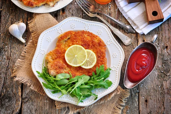 Schweineschnitzel mit Bio-Rucola und Limette auf altem Holzgrund. — Stockfoto