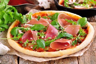 Ev yapımı pizza domates sosu, mozzarella peyniri, organik roka, Parma jambonu, Kapari ve parmesan peyniri ile.