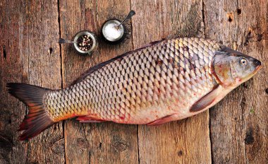 Fresh raw wild carp with sea salt and pepper on old wooden background. clipart