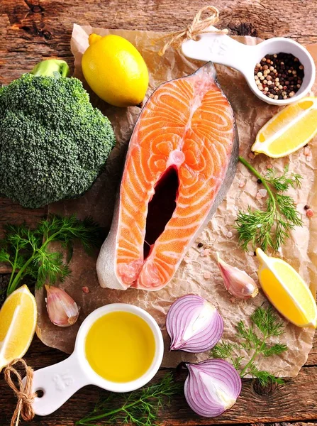 Rauwe zalm met broccoli, citroen, knoflook, rode ui, dille, olijfolie en Himalayazout op de oude houten achtergrond. Gezonde voeding. — Stockfoto