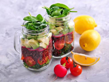 Sağlıklı salata quinoa, avokado, domates, kırmızı soğan, Bebek ıspanak, turp ve zeytinyağında bir Mason ile kavanozlar.