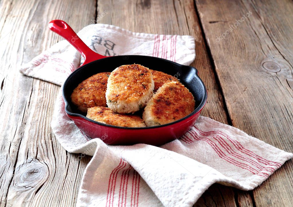 Chicken cutlets( burgers) in a cast iron skillet over an old wooden background.