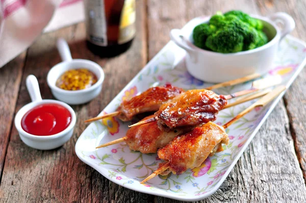 Delicious chicken kebab on wooden skewers with boiled broccoli on the old wooden background.