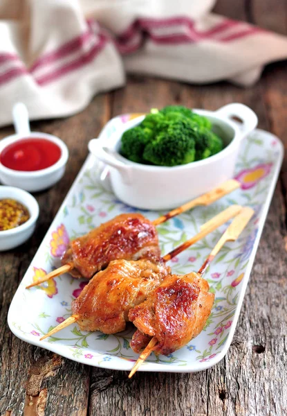 Delicious chicken kebab on wooden skewers with boiled broccoli on the old wooden background.