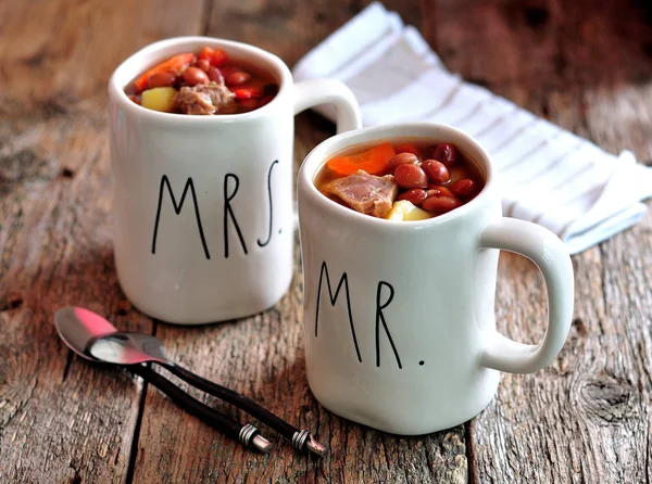 Köstliche Rindfleischsuppe mit Zwiebeln, Kartoffeln, Karotten und roten Bohnen in Tassen auf altem Holzgrund. — Stockfoto