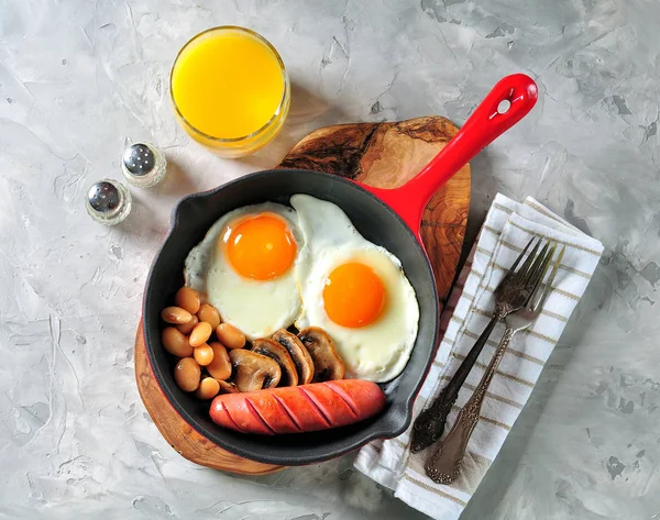 Petit déjeuner classique avec œufs frits, saucisses, champignons, haricots dans une poêle en fonte . — Photo