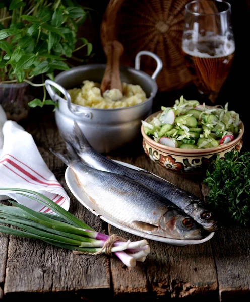 Salted herring with mashed potatoes and cucumber salad, radish and cabbage with olive oil on an old wooden background. Rustic style. — Stock Photo, Image