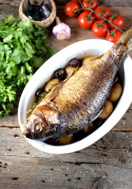 Baked golden fish with carp with potatoes and mushrooms on an old wooden background. Rustic style. clipart