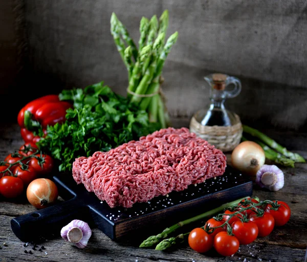 Fresh raw ground beef with fresh vegetables on an old wooden background. Rustic style.
