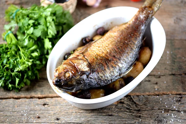 Baked golden fish with carp with potatoes and mushrooms on an old wooden background. Rustic style. — Stock Photo, Image