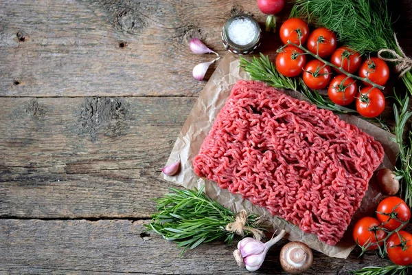 Färsk rå köttfärs nötkött med rosmarin, dill, vitlök och körsbärstomater på en gammal trä bakgrund. Kopiera utrymme, — Stockfoto