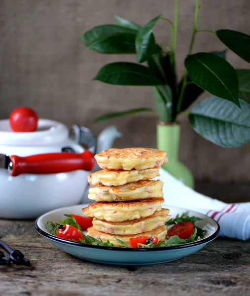 Pancakes with cheese, ham fresh vegetables and arugula on an old wooden background. Rustic style.