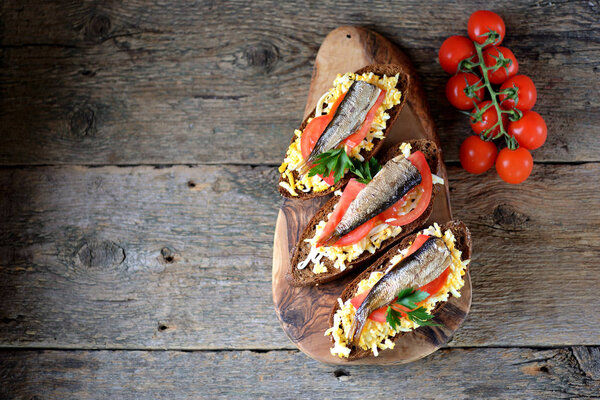 French toast with sprats, boiled egg, tomato, garlic and mayonnaise on an olive serving board.  Top view. Copy space. 