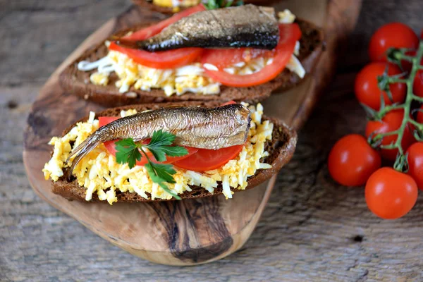 Французские тосты со шпротами, вареным яйцом, помидорами, чесноком и майонезом на доске для подачи оливок . — стоковое фото